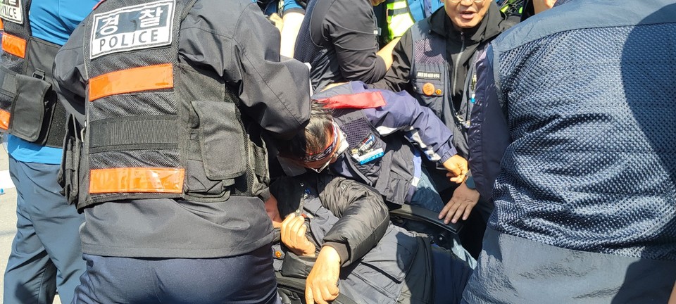 경찰이 화물트럭 통행로를 확보하기 위해 농성을 하고 있는 노동자들을 밀치고 있다.